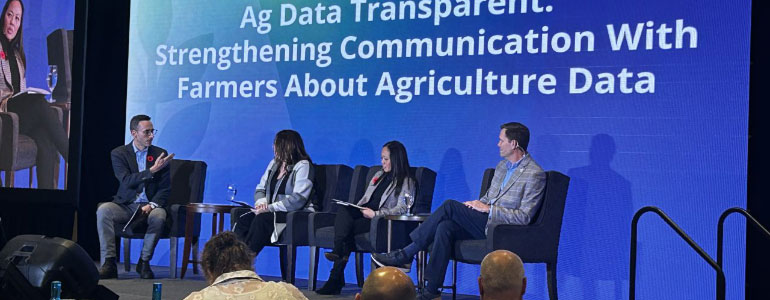 Panel members sitting in chairs on stage with video screen in background