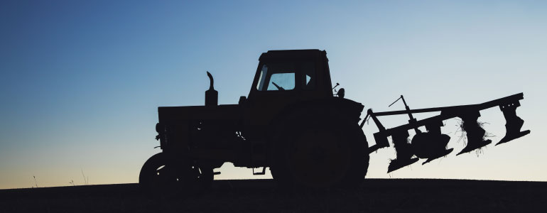 Silhouette of a tractor on a field against a blue sky