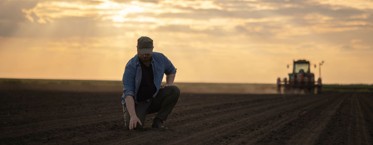 Farmer kneeling in soil next to tractor